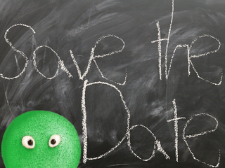 Eine Tafel mit der Aufschrift "Save the Date", eine grüne Figur schaut über den Bildrand